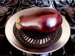 Pierced eggplant on top of grill pan on stovetop.