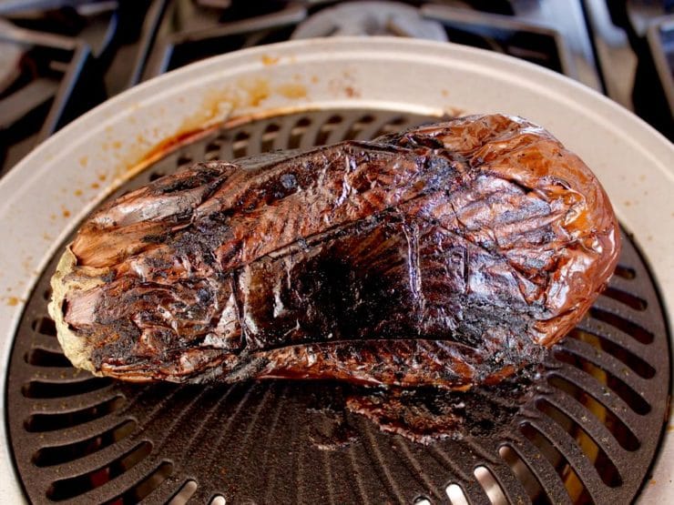 Smoky collapsing grilled eggplant on grill pan on stovetop.