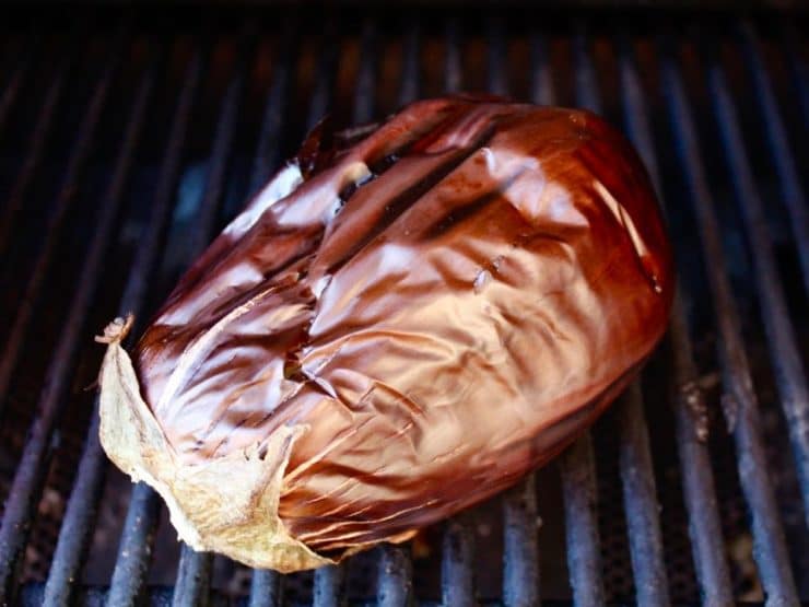 A whole eggplant grilling on a barbecue, showing charred and blistered skin