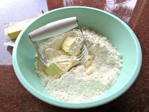 Cutting butter into flour in a bowl with a pastry cutter.