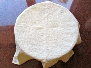 Dough in a bowl covered with a damp towel.