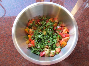 Chopped basil added to tomatoes in mixing bowl.