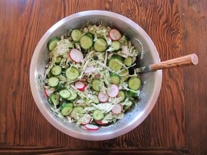 Tossing salad with dressing in a large bowl.