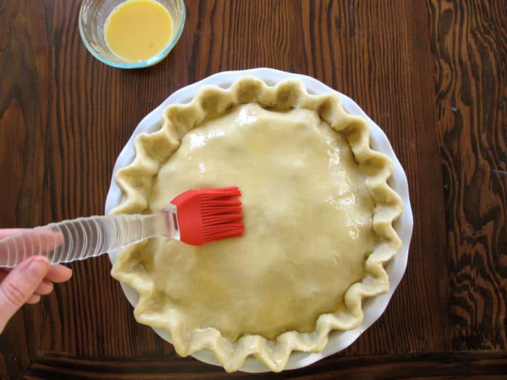 Brushing eggwash on top pie crust.