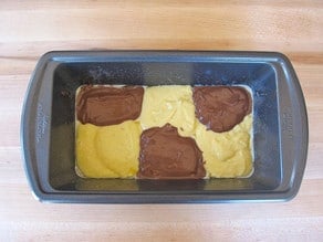 Small rectangular cake pan with three dollops of yellow batter staggered with three dollops of brown batter.