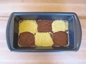 Small rectangular cake pan with three dollops of yellow batter staggered with three dollops of brown batter, second layer.