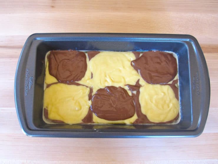 Small rectangular cake pan with three dollops of yellow batter staggered with three dollops of brown batter, third layer.