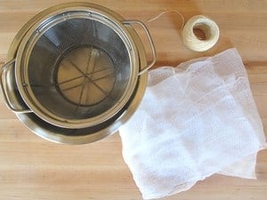 Mesh strainer, kitchen twine and cheesecloth on wooden cutting board.