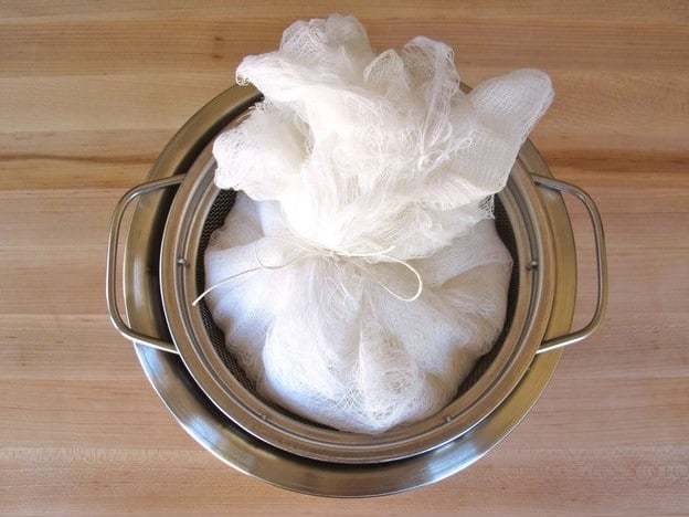 Yogurt in cheesecloth-lined mesh colander, tied up with kitchen twine into bundle.