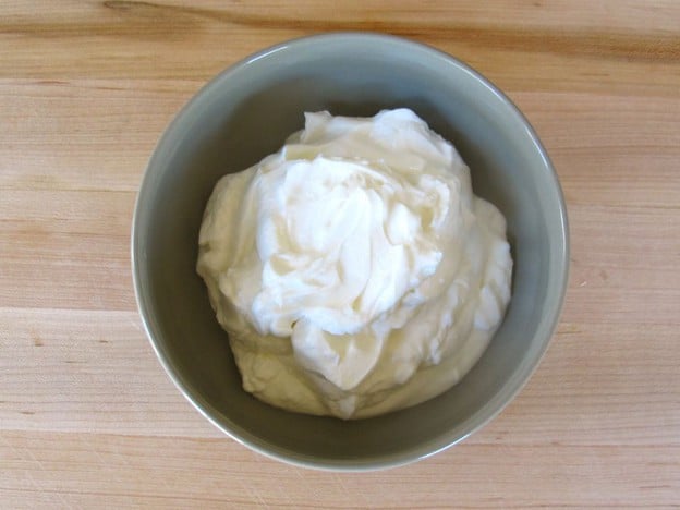 Thickened strained yogurt in bowl on cutting board.