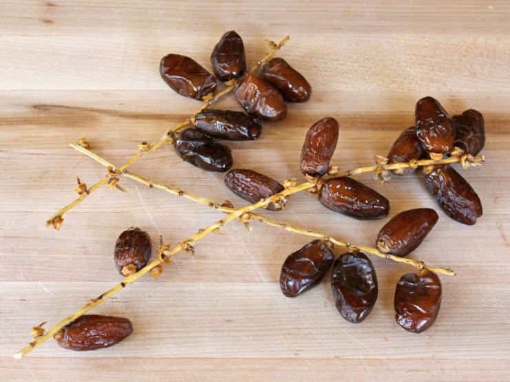 Three small branches of juicy ripe dates on a wooden cutting board.