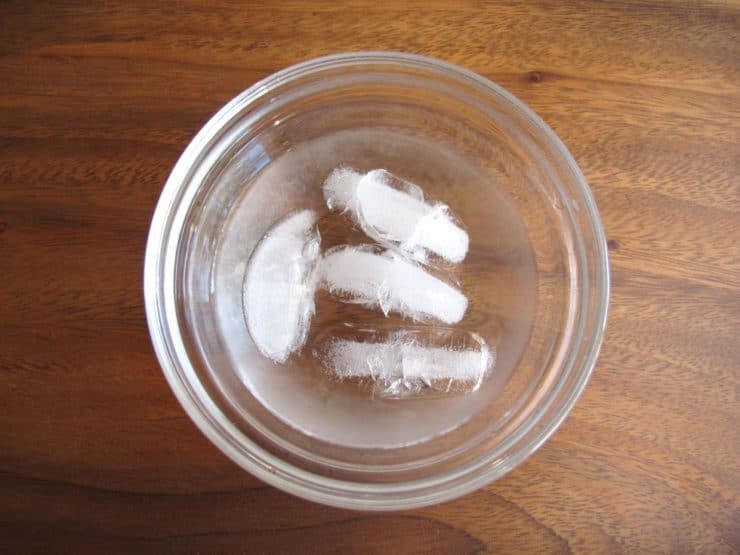 Ice cubes in a glass bowl, ready for use in an ice water bath to aid in cooking preparations