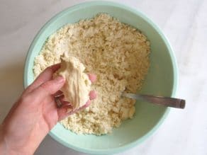 Hand holding flour butter mixture compressed into dough over mixing bowl with fork.