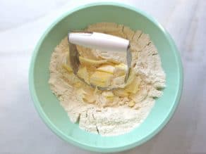 Cutting butter into dry ingredients in mixing bowl on marble background.
