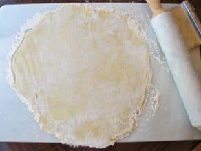 Pie crust dough rolled out on marble surface with rolling pin and flour.