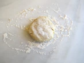 Ball of pie crust dough dusted with flour on marble surface.