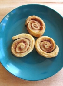 Three pie crust pinwheels on plate with wooden background.