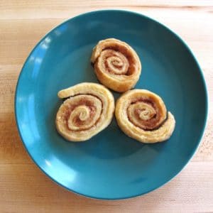 Three pie crust pinwheels on plate with wooden background.