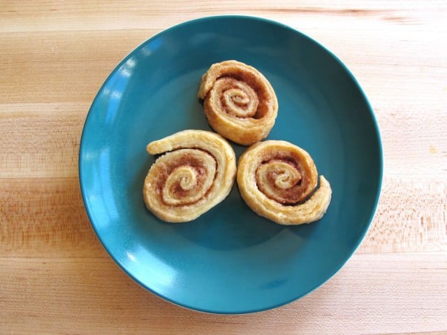 Three pie crust pinwheels on blue plate on wooden cutting board.