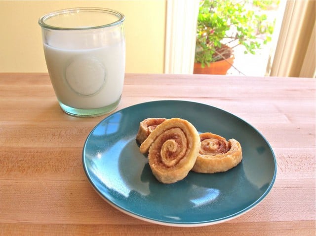 Three pie crust pinwheel treats on a blue plate on wooden cutting board with glass of milk.