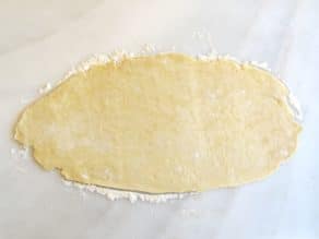 Pie crust dough with flour on marble surface.