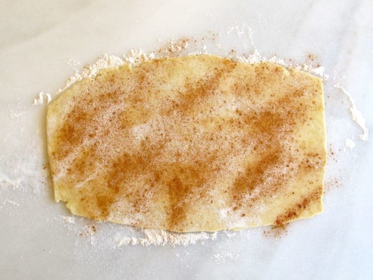 Pie crust pinwheel dough filled with sugar on marble surface.
