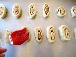 Brusing pie crust pinwheels with melted butter on baking sheet.