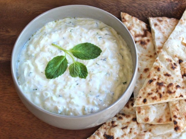 A horizontal shot of Tzatziki Sauce on a white bowl with pita bread on side