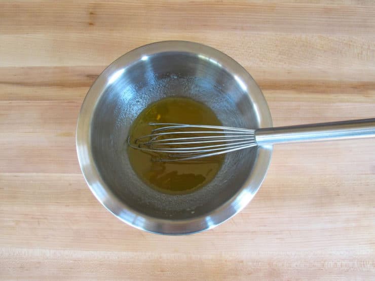 Whisking olive oil and honey marinade in a small bowl.