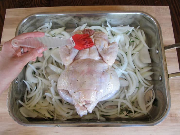 Whole chicken, breast side down on a bed of sliced onions in a baking dish.