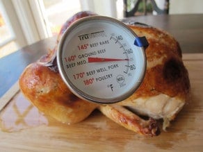 Meat thermometer in whole chicken on a cutting board.