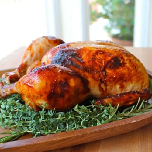 A whole honey herb roasted chicken with herbs on a wooden plate