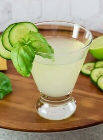 Vertical shot of a short cocktail glass filled with a cucumber martini recipe, garnished with slices of fresh cucumber.