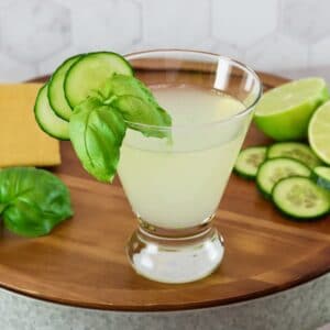 Vertical shot of a short cocktail glass filled with a cucumber martini recipe, garnished with slices of fresh cucumber.