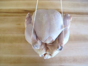 Whole chicken on cutting board - trussing strings wrapped around drumsticks.