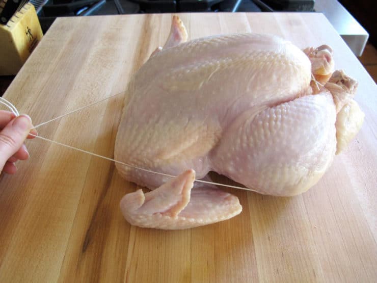 Side view of whole chicken on cutting board - trussing strings pulled alongside the chicken over wings.