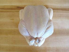 Fully trussed chicken on wooden cutting board.