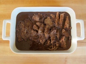Sliced brisket in a serving dish with molasses.