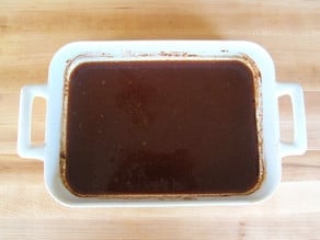 Water added to pomegranate molasses in a baking dish to thin.
