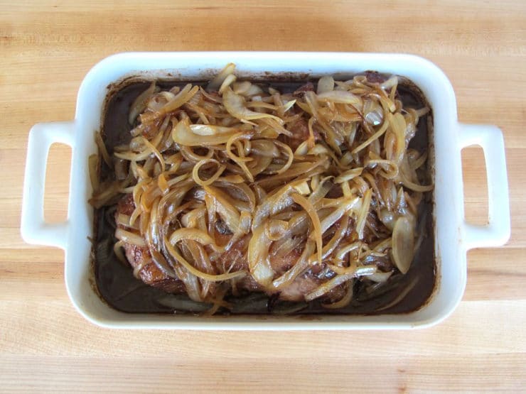 Browned onions poured over brisket in roasting pan.