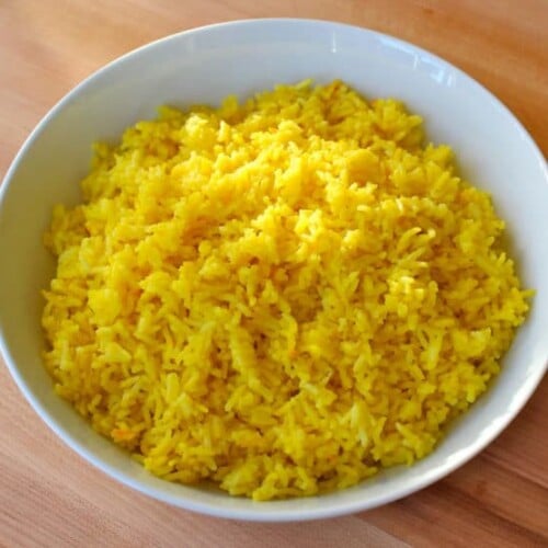 Horizontal close up shot of Saffron rice in a white bowl on top of a wood table.