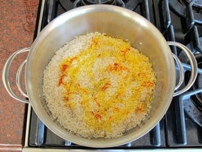 Saffron water added to cooked rice in a saucepan.