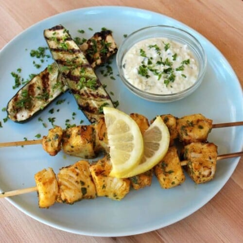 Grilled fish skewers with Mediterranean flavors on a plate with grilled eggplants and lemons