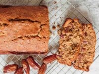 Featured square shot - sliced date honey nut cake on cooling rack with luscious dates on marble countertop.