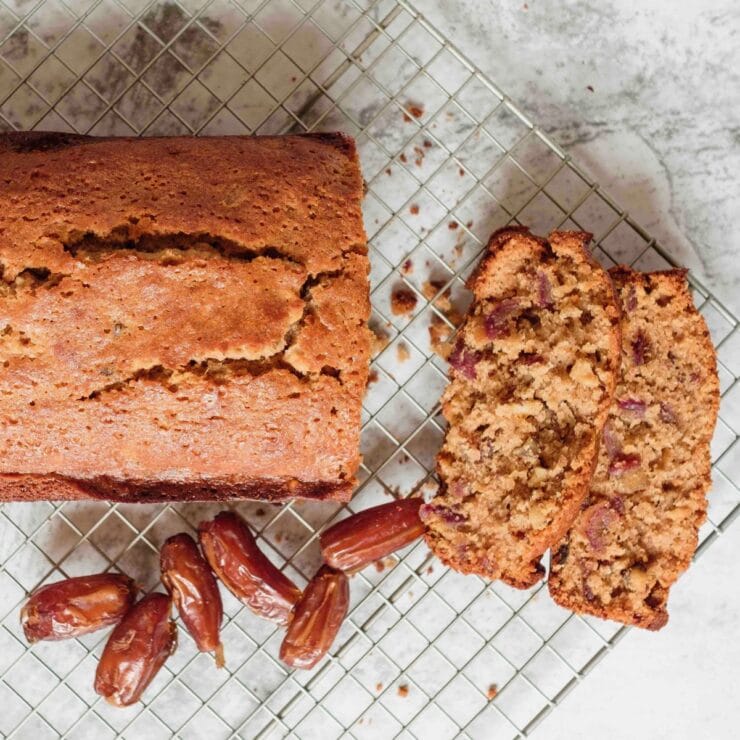 Featured square shot - sliced date honey nut cake on cooling rack with luscious dates on marble countertop.