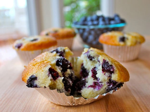 Blueberry muffin filled with blueberries and a side of fresh blueberries in a bowl