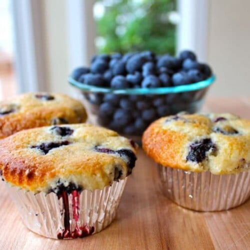 Three blueberry muffins with a side of fresh blueberries