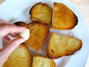 Scraping a garlic clove on toasted challah slices.