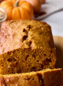 Featured Square Crop - Pumpkin Spice Cake Loaf on Cutting Board with pumpkin, raisins and spices in background on marble countertop.