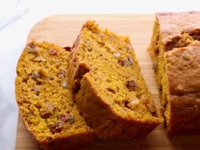 Front View - sliced pumpkin spice cake loaf on a wooden cutting board on marble countertop.